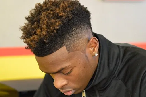Cheveux frisés avec mèches cuivrées et taper fade, contour précis