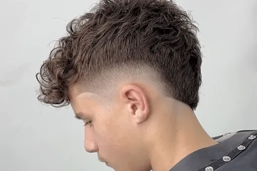 Mullet moderne bouclé avec burst fade autour de l’oreille
